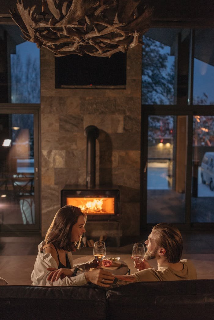 A couple enjoying wine by a warm fireplace, creating a cozy ambiance in winter.